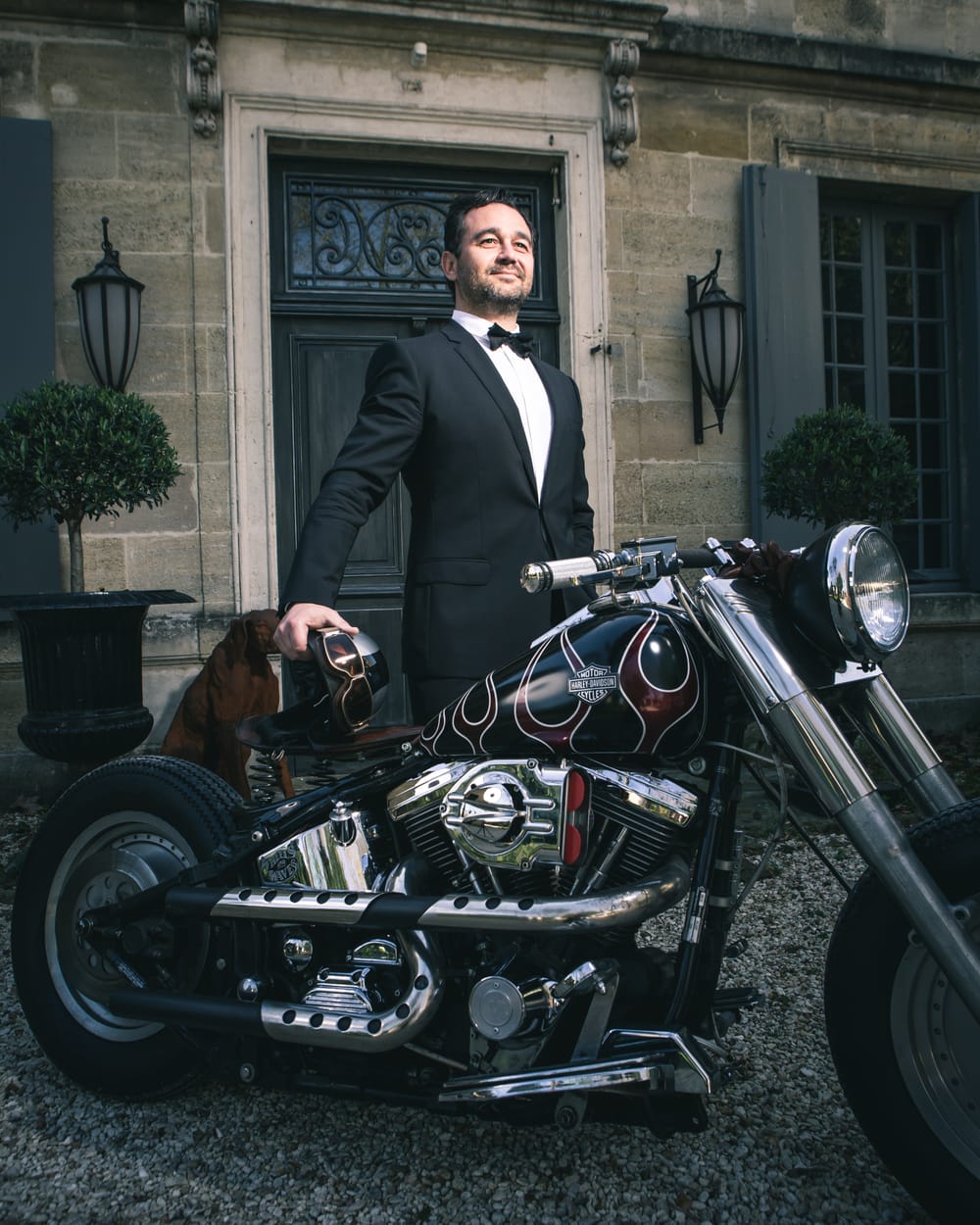 Olivier Chadebost en smoking, à côté d'une moto devant une demeure