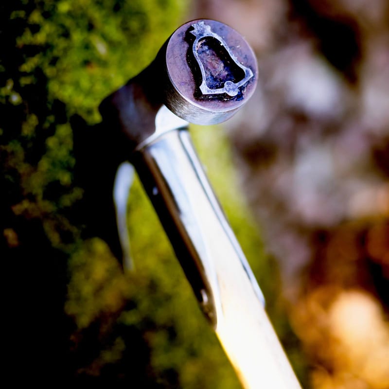 Head of a forestry hammer engraved with a bell, in the undergrowth light