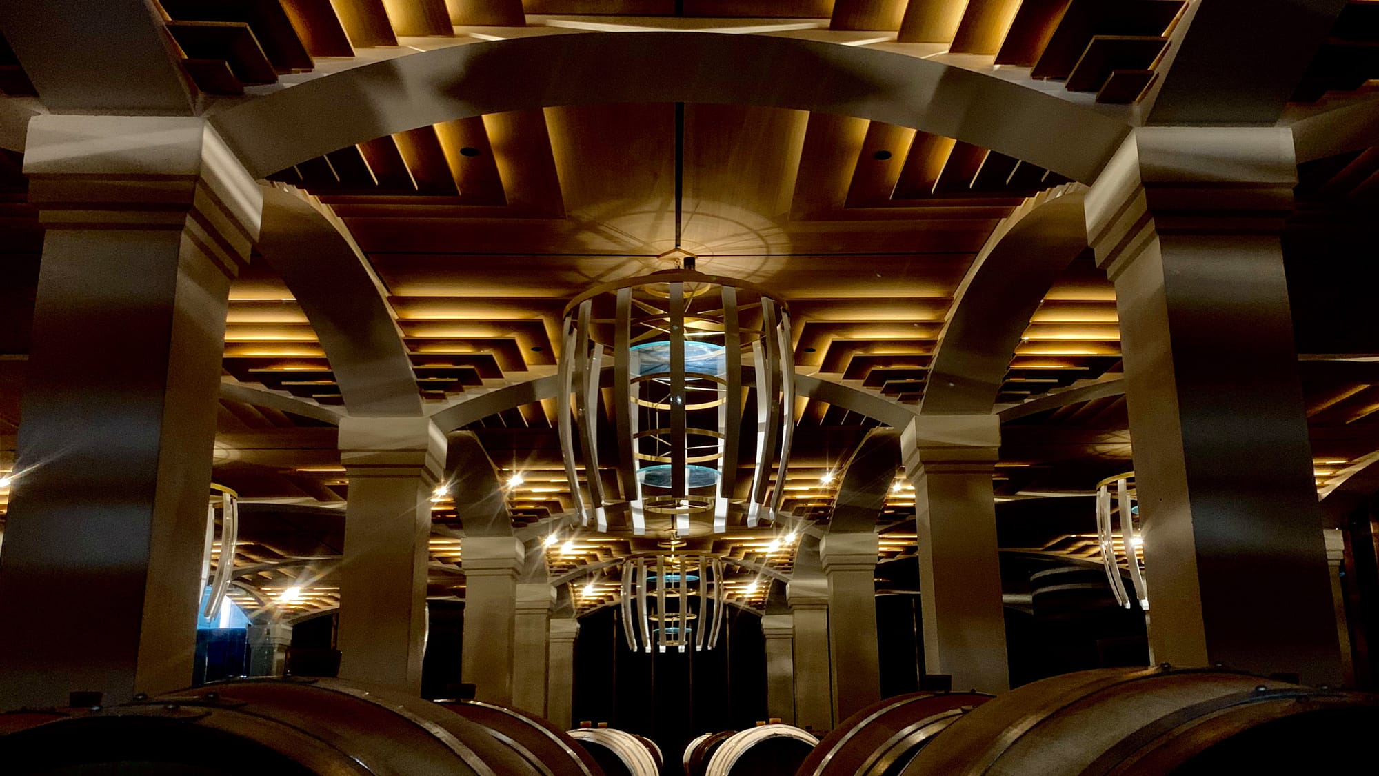 Chai sous une voûte à caissons de bois, cuves et barriques éclairées