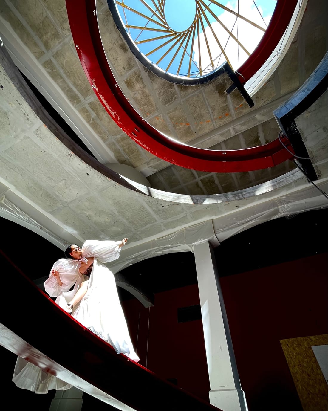 Danseuse en robe blanche sous la verrière et la rampe rouge d'un escalier