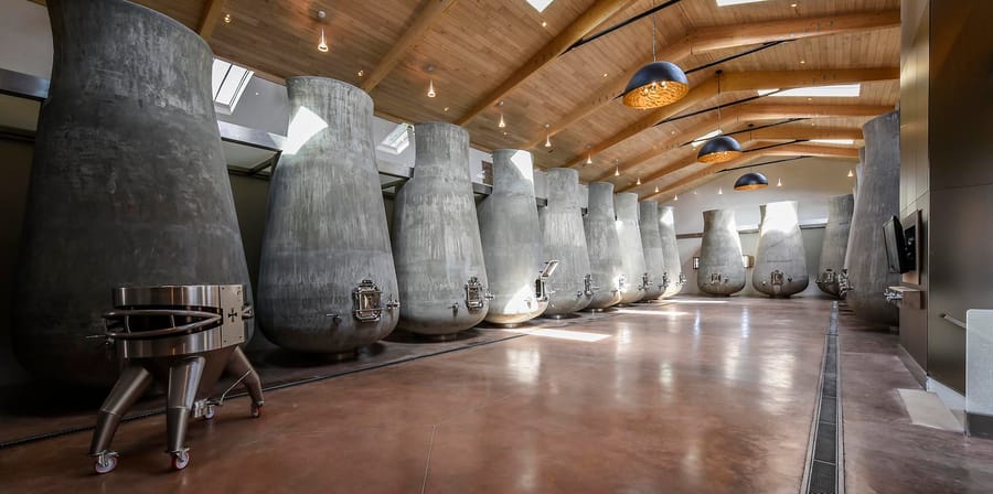Alignement de cuves tronconiques en béton dans un cuvier contemporain sous un plafond en bois, au sein d'un domaine viticole, Château Beauregard à Pomerol