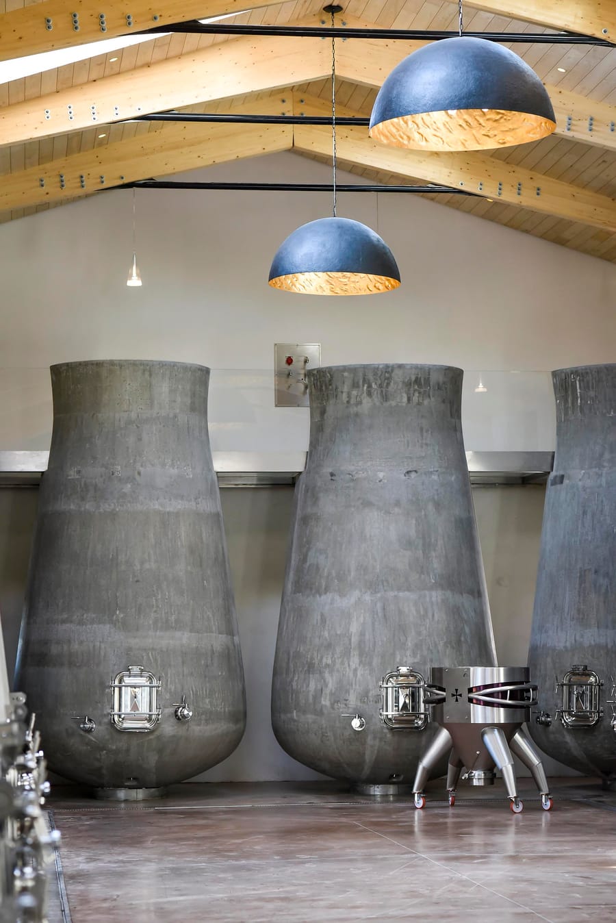 Grandes cuves en béton sous la charpente en bois d'un chai de vinification moderne, Château Beauregard à Pomerol