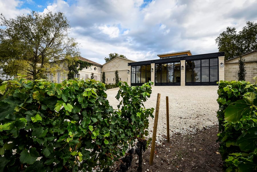 Vignes au premier plan devant un bâtiment moderne en verre et pierre d'un domaine viticole, Château Beauregard à Pomerol