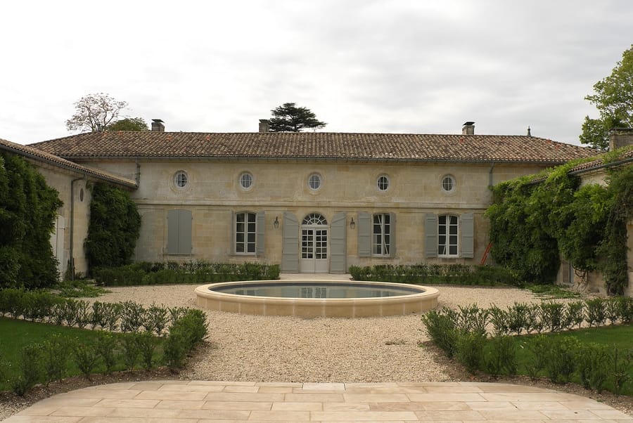 Façade en pierre d'une demeure et son bassin circulaire au centre d'une cour gravillonnée au Château Beauregard, à Pomerol