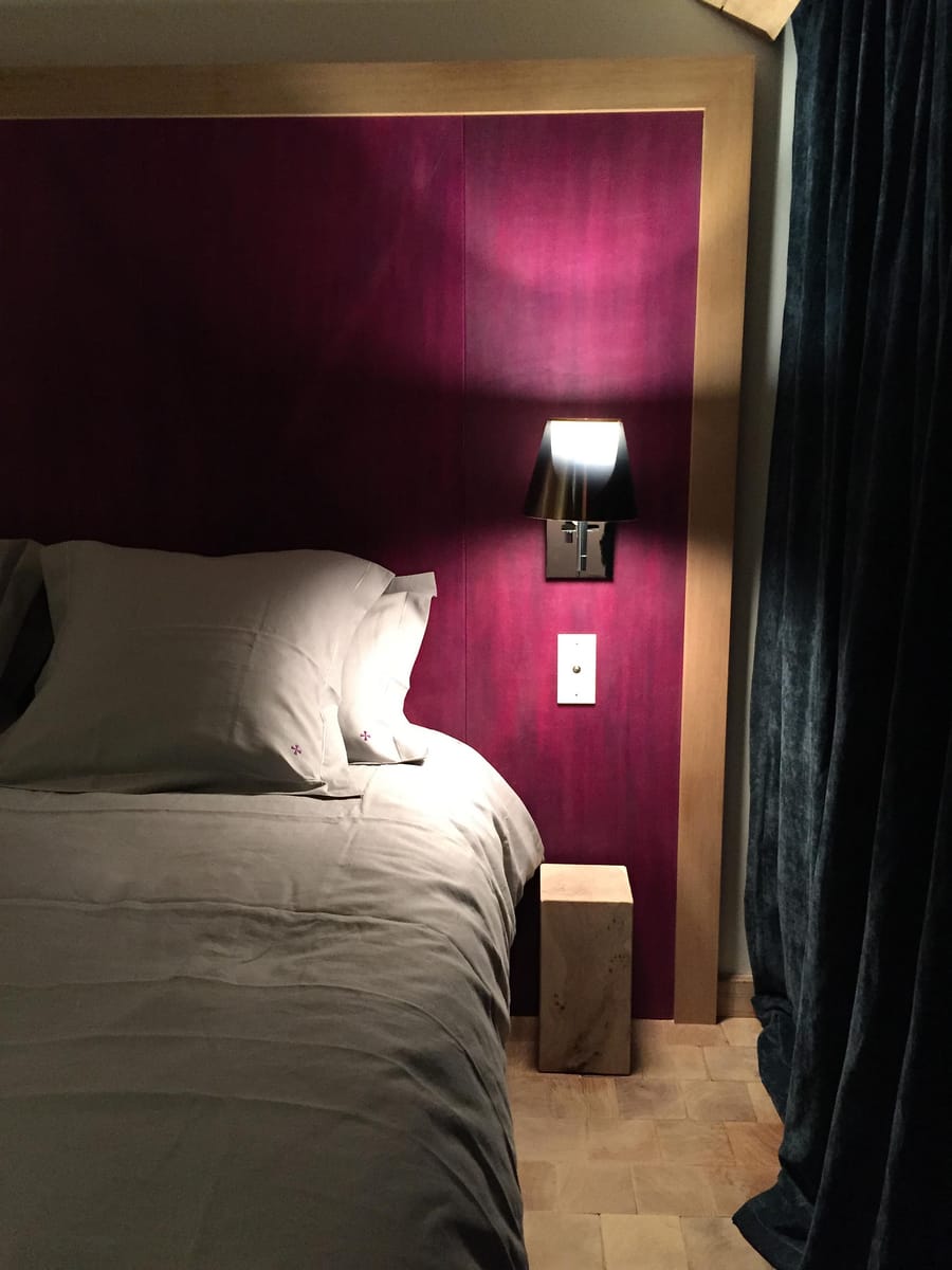 Lit fait avec des oreillers devant une grande tête de lit pourpre éclairée par une applique au Château Beauregard