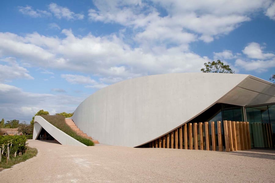 Bâtiment contemporain en béton blanc aux formes ondulées et toit végétalisé, bordé par un vignoble à Saint-Émilion