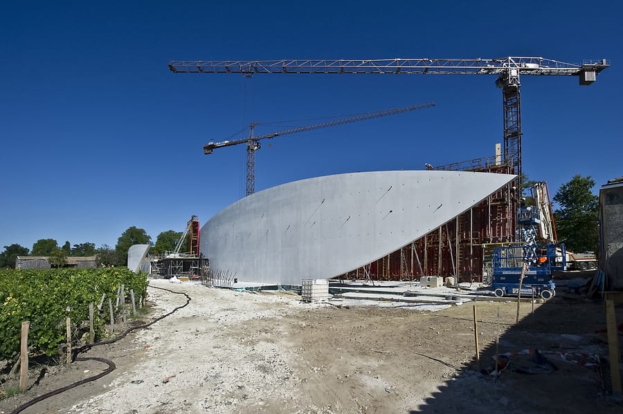 Chantier de construction d'un chai viticole contemporain en béton avec des grues au bord des vignes, Château Cheval Blanc à Saint-Émilion