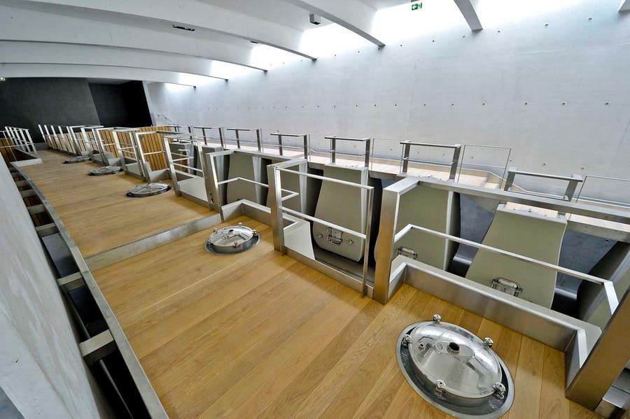 Passerelle en bois et garde-corps en inox surplombant des cuves de vinification dans un chai contemporain, Château Cheval Blanc à Saint-Émilion