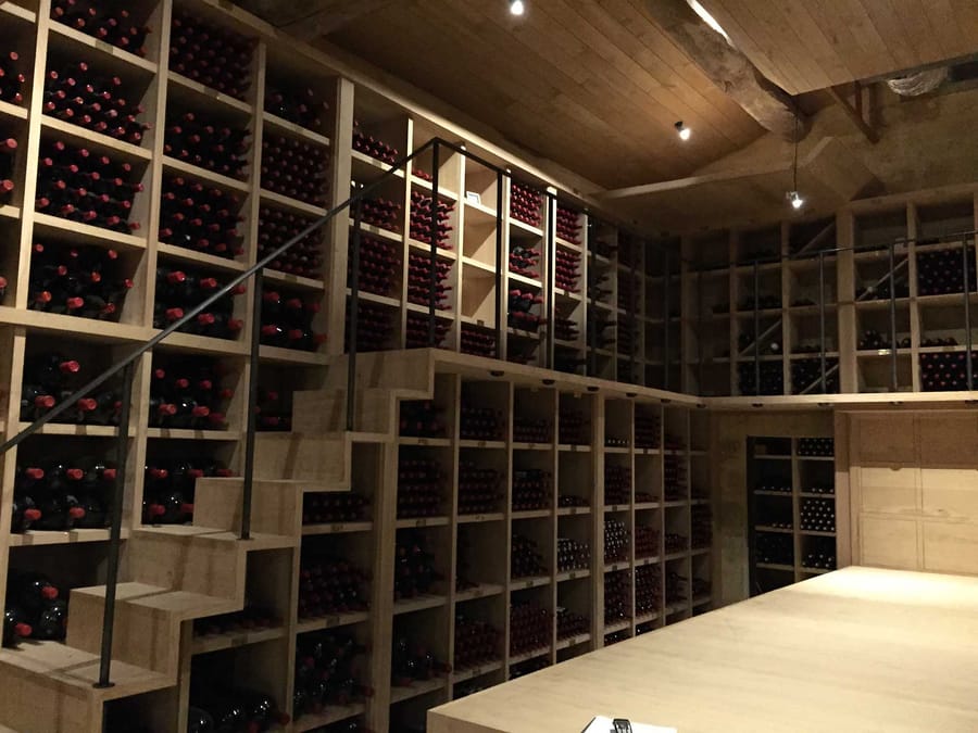 Casiers en bois remplis de bouteilles de vin organisés sur deux niveaux avec un escalier dans une cave, Château Cheval Blanc à Saint-Émilion