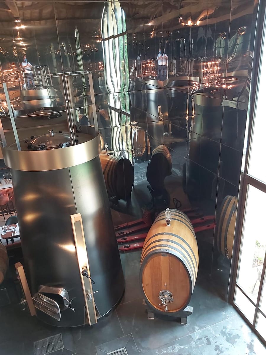 Alambic en métal sombre et fût de chêne dans une distillerie contemporaine aux parois réfléchissantes à La Gaude