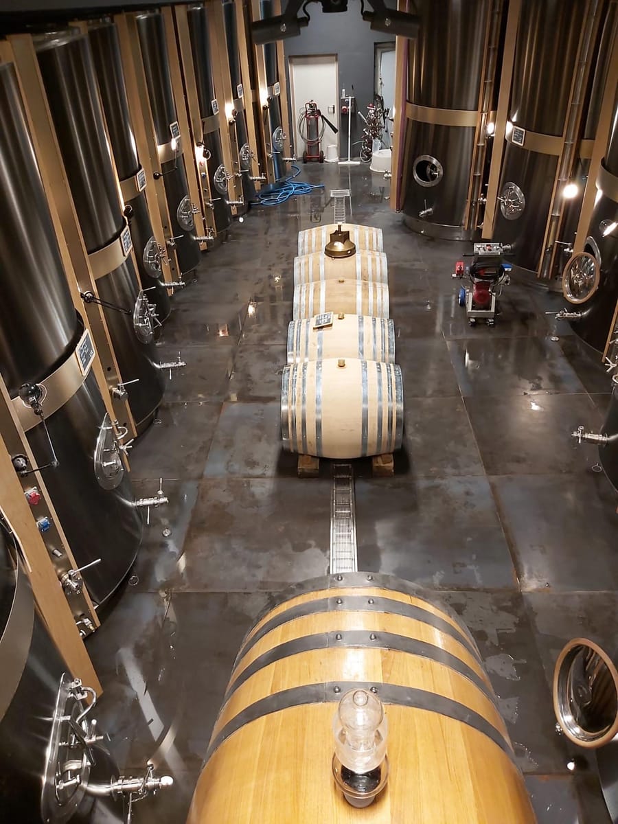 Alignement de fûts en bois et de cuves en inox dans un chai de vinification à La Gaude