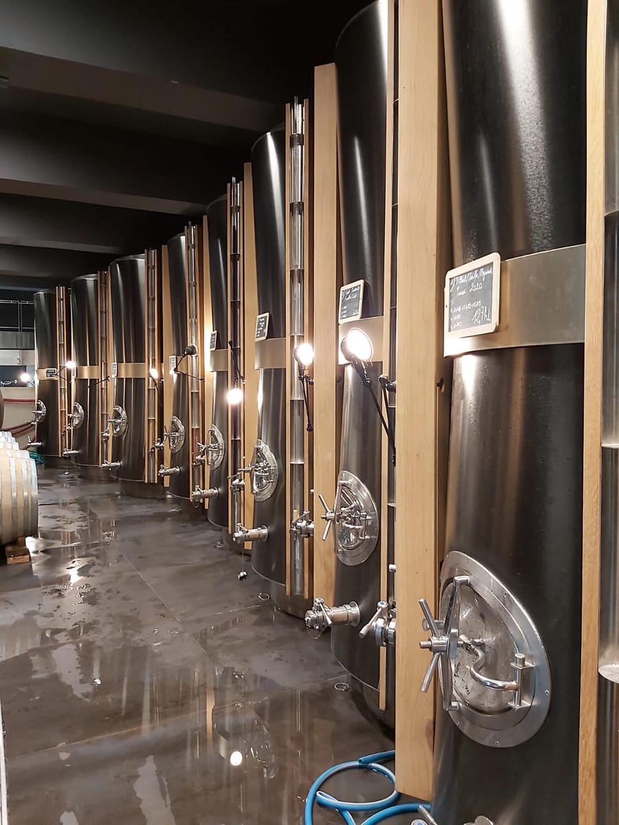 Alignement de grandes cuves de vinification métalliques et bois dans la cuverie d'un domaine viticole à La Gaude