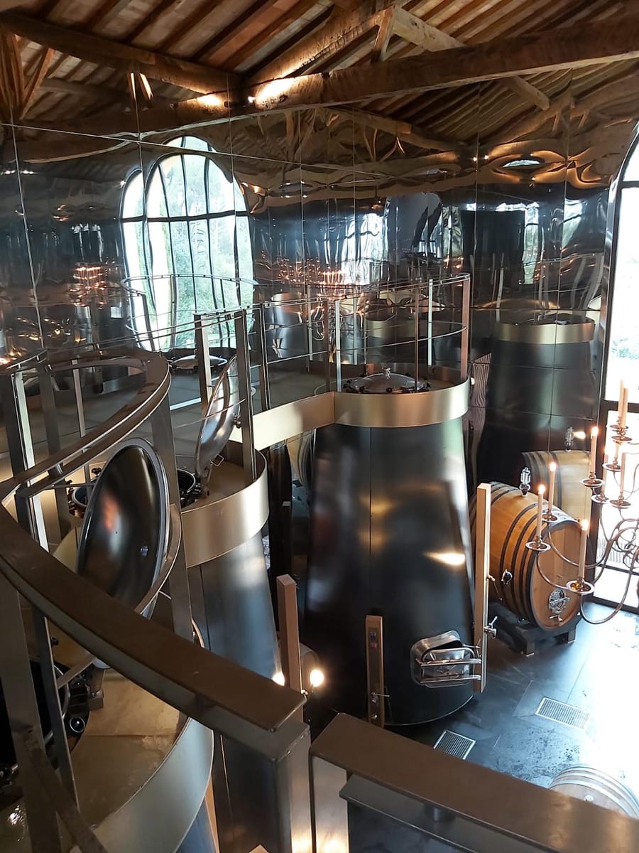 Cuves en inox et fûts en bois au sein d'un chai moderne aux parois réfléchissantes, à La Gaude