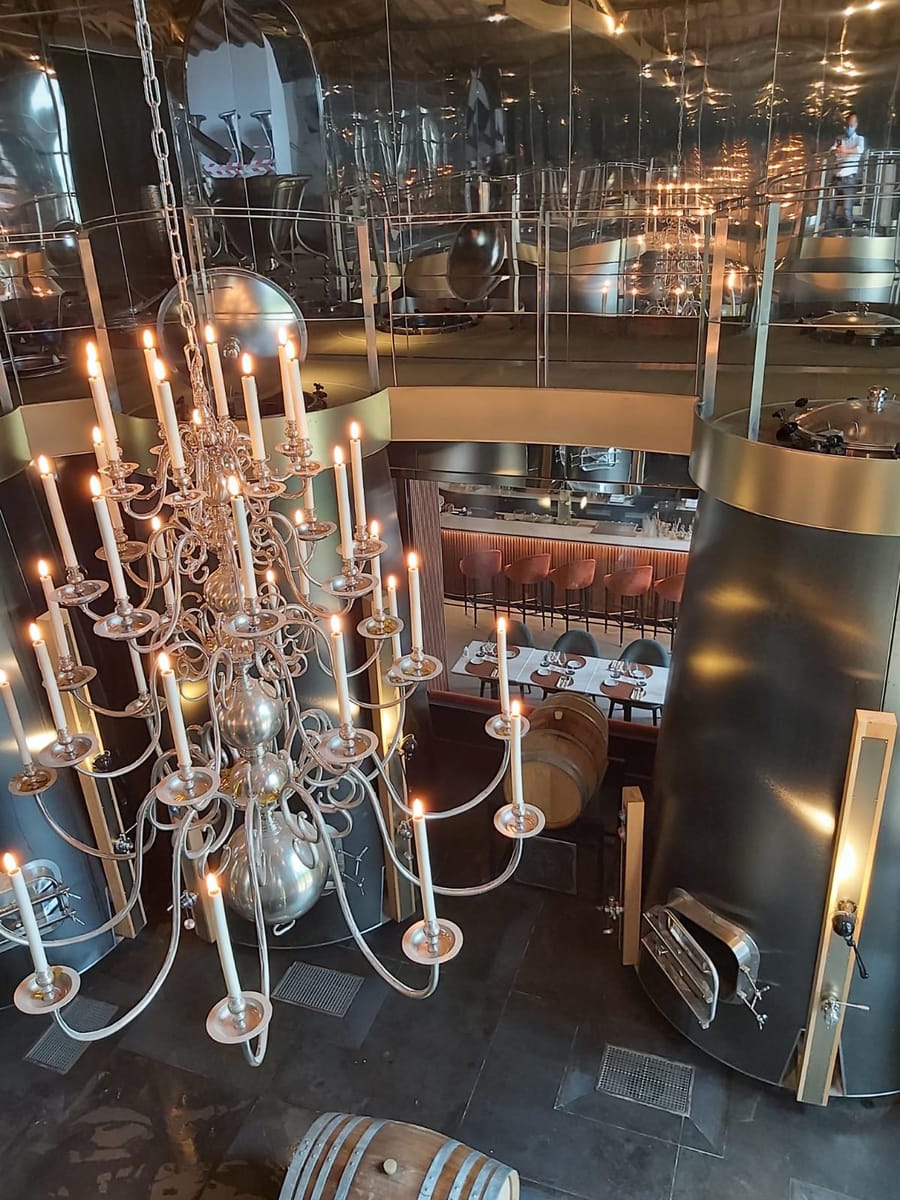 Grand lustre argenté éclairant un chai moderne aménagé avec des cuves métalliques et des barriques, à La Gaude