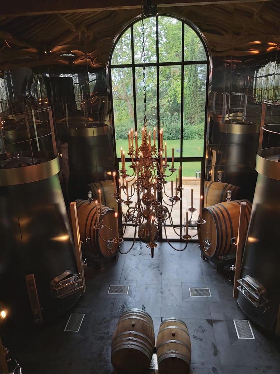 Intérieur d'un chai contemporain avec fûts de vin en bois et grand lustre suspendu devant une baie vitrée à La Gaude