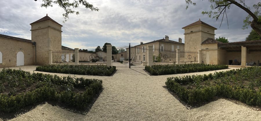 Allée gravillonnée menant à la grille en fer forgé et aux bâtiments en pierre d'un domaine restauré, Château de Sours dans l'Entre-deux-Mers
