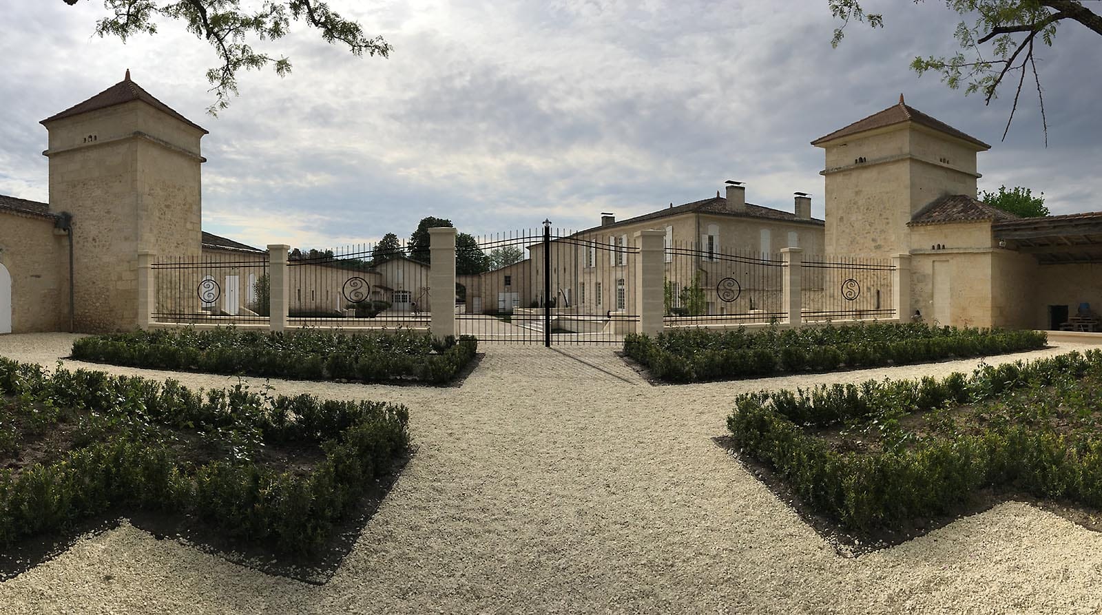 Allées en gravier et parterres taillés menant au portail en fer forgé d'un domaine en pierre à Sours