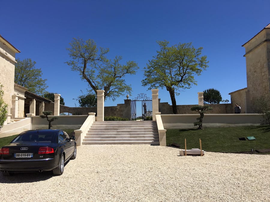 Voiture noire garée devant un escalier en pierre menant au portail d'une propriété avec une cour en gravier à Sours
