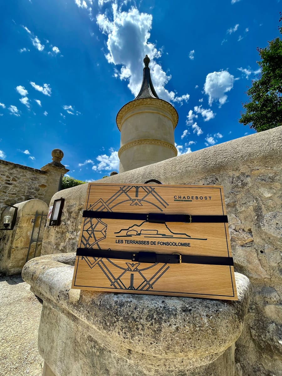 Coffret en bois gravé Chadebost avec sangles en cuir posé sur une structure en pierre devant une tour du Château de Fonscolombe