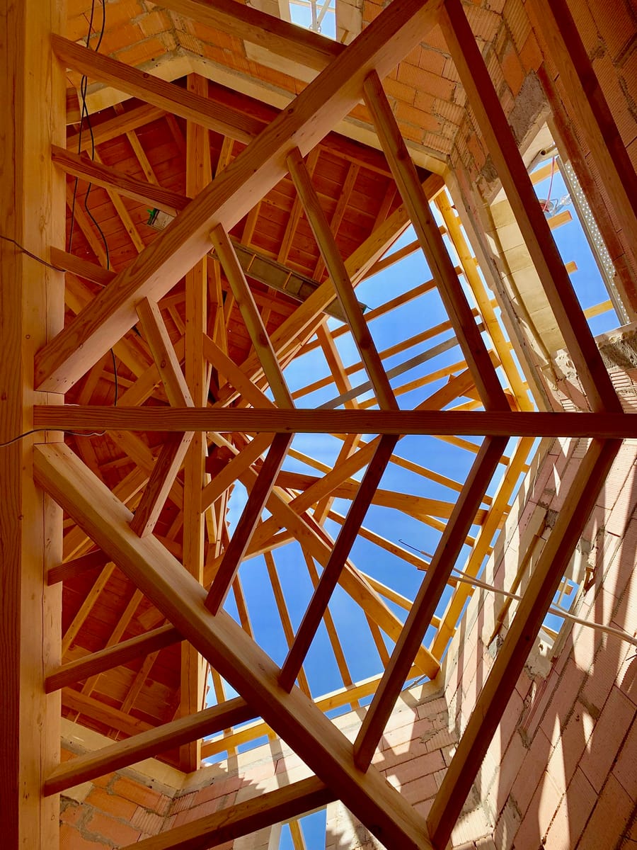 Vue de dessous d'une charpente en bois en cours d'assemblage sous un ciel bleu, sur un chantier d'architecture, Château Grand Pontet à Saint-Émilion