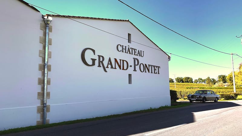 Façade blanche du bâtiment du Château Grand-Pontet avec une voiture de collection garée près des vignes, Château Grand Pontet à Saint-Émilion