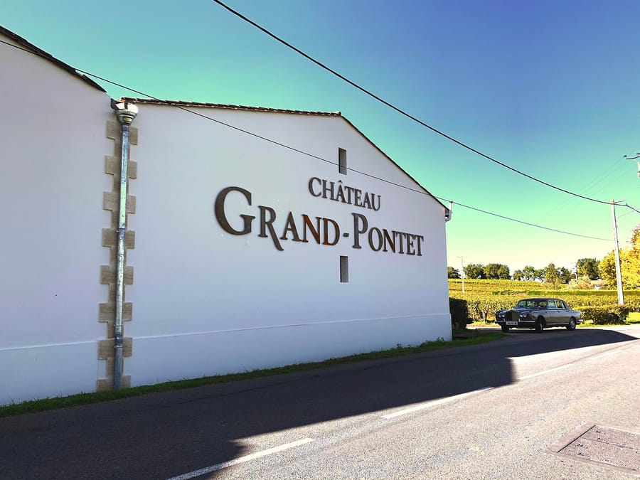 Façade blanche d'un bâtiment avec l'inscription Château Grand-Pontet et une voiture ancienne devant les vignes, Château Grand Pontet à Saint-Émilion