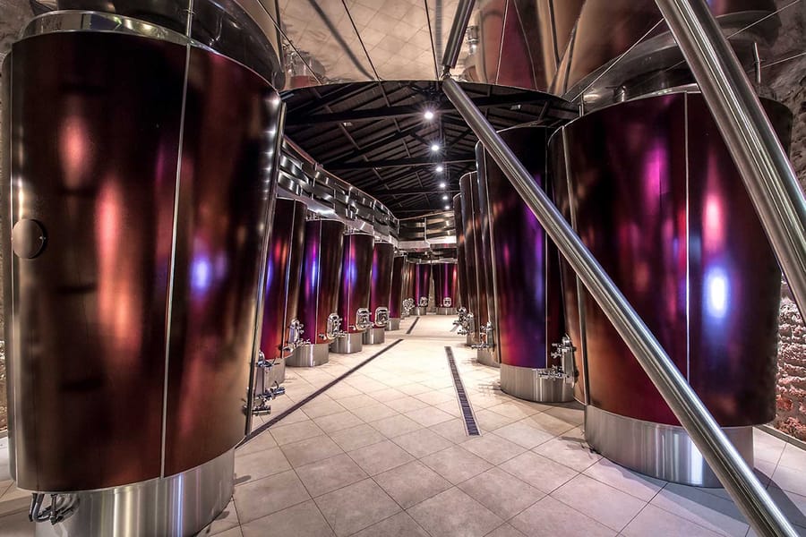 Alignement de grandes cuves en inox aux reflets pourpres dans un cuvier contemporain, Château La Gaffelière à Saint-Émilion