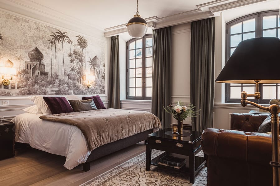 Chambre à coucher élégante avec lit double, papier peint panoramique et fauteuil en cuir, aménagée par un architecte, Château Laffitte Carcasset à Saint-Estèphe