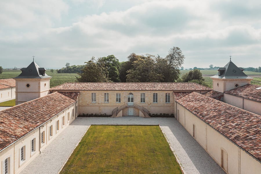 Cour intérieure rectangulaire d'un domaine viticole restauré entourée de bâtiments en pierre et de vignes, Château Laffitte Carcasset à Saint-Estèphe