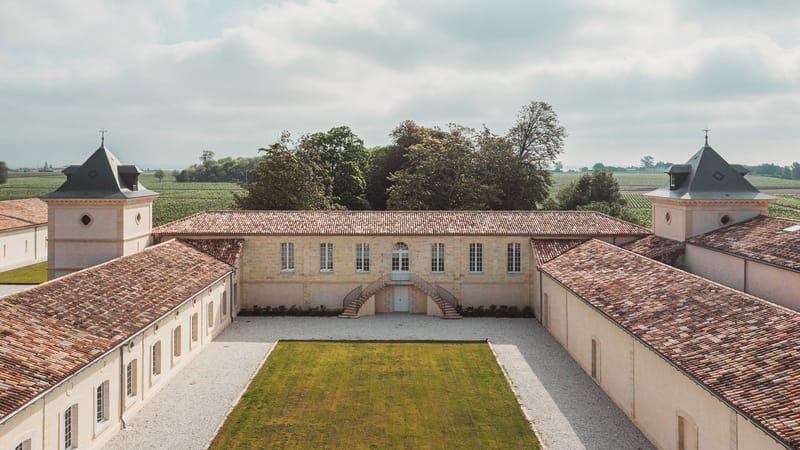 Vue en hauteur de la cour intérieure d'un domaine viticole aux bâtiments en pierre entouré de vignes, Château Laffitte Carcasset à Saint-Estèphe