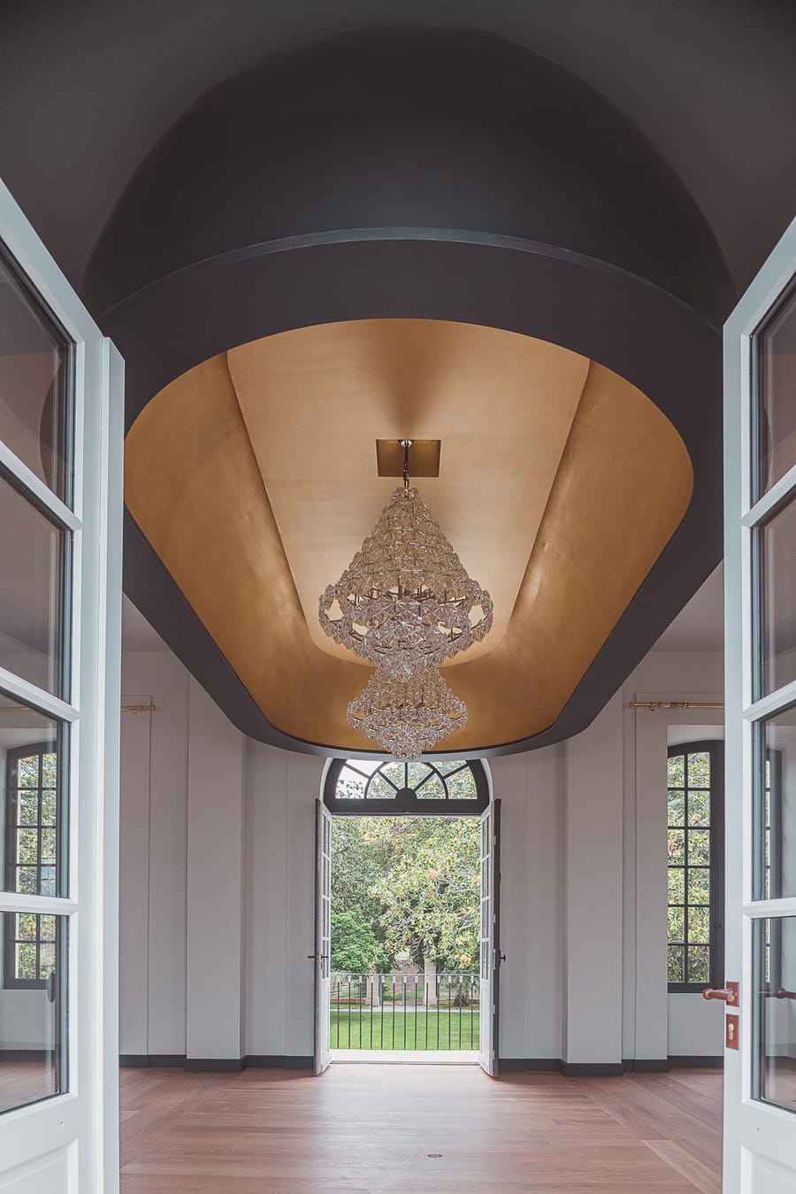 Lustre en cristal suspendu sous un plafond alvéolé doré dans une pièce élégante ouvrant sur le parc, Château Laffitte Carcasset à Saint-Estèphe