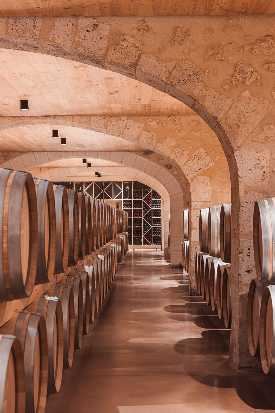 Alignement de barriques en bois sous des voûtes en pierre dans un chai viticole, Château Laffitte Carcasset à Saint-Estèphe