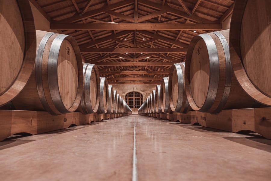 Alignement symétrique de grands tonneaux en bois dans un chai de vieillissement à la charpente apparente, Château Laffitte Carcasset à Saint-Estèphe