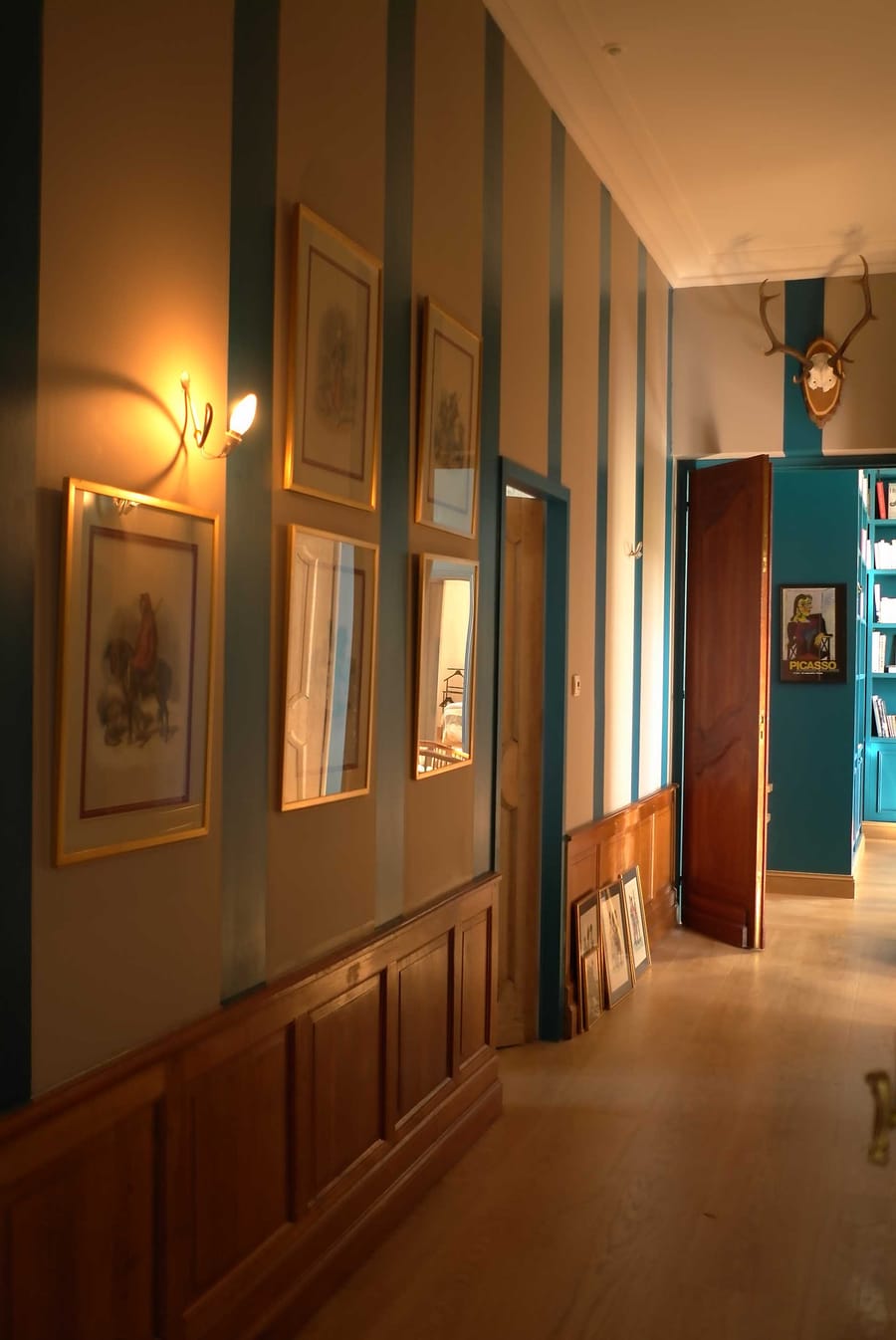 Couloir aux murs rayés bleu et beige ornés de cadres, avec un soubassement en bois au Château Lafon-Rochet