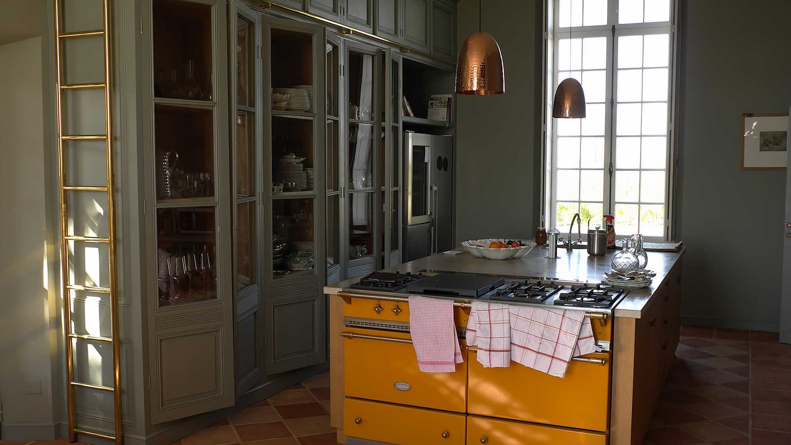 Cuisine aménagée avec un piano de cuisson jaune, un îlot central et des placards vitrés gris, dans un château, Château Lafon-Rochet à Saint-Estèphe