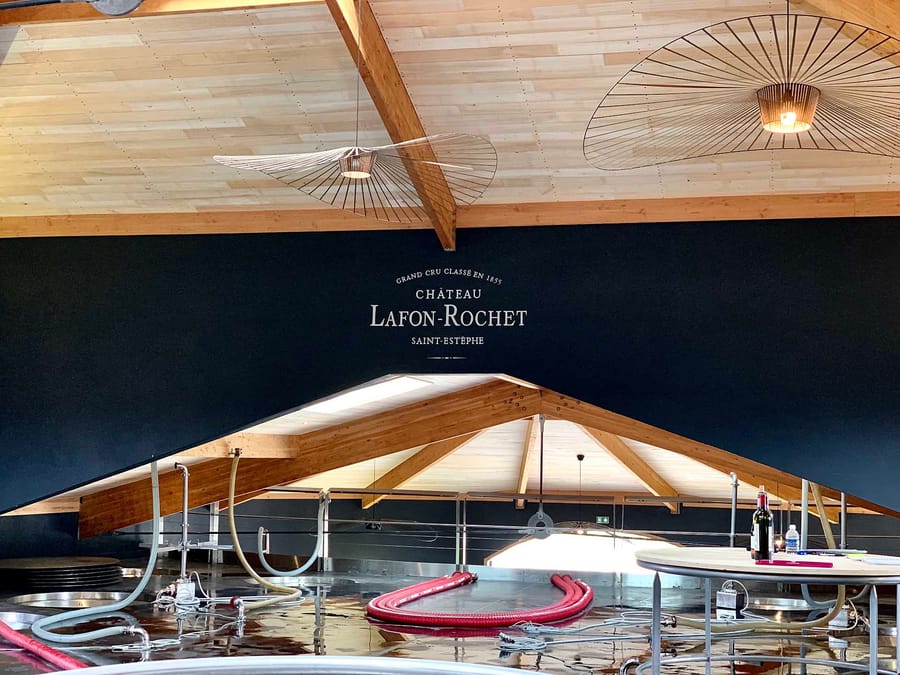 Cuvier contemporain éclairé par des suspensions design sous une charpente en bois au Château Lafon-Rochet à Saint-Estèphe