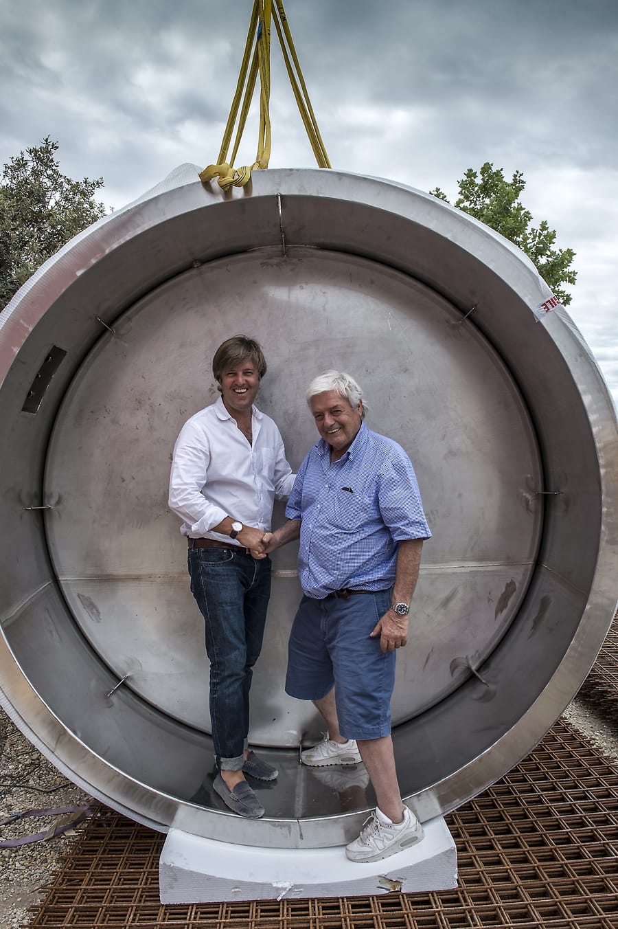 Deux hommes se serrant la main à l'intérieur d'une grande cuve en inox sur le chantier d'un domaine viticole, Château Lafon-Rochet à Saint-Estèphe
