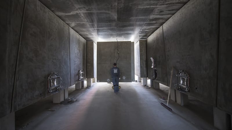 Un ouvrier debout dans l'allée centrale d'un cuvier contemporain entouré de cuves en béton, dans un domaine viticole, Château Lafon-Rochet à Saint-Estèphe