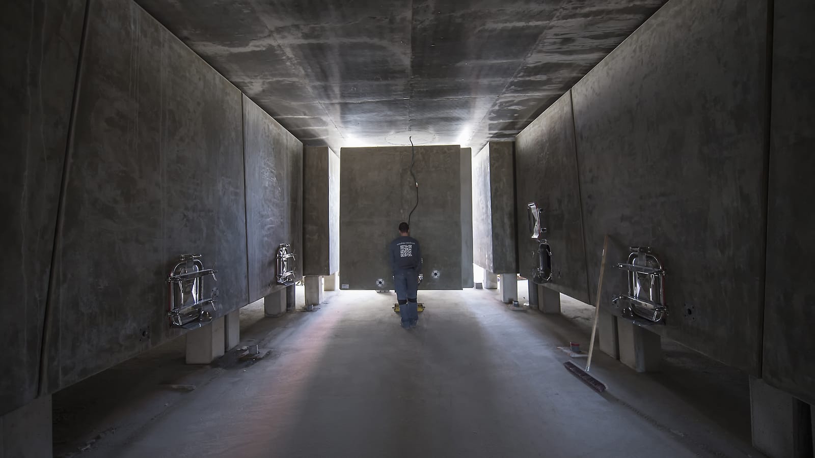 Un ouvrier debout dans l'allée centrale d'un cuvier contemporain entouré de cuves en béton, dans un domaine viticole, Château Lafon-Rochet à Saint-Estèphe