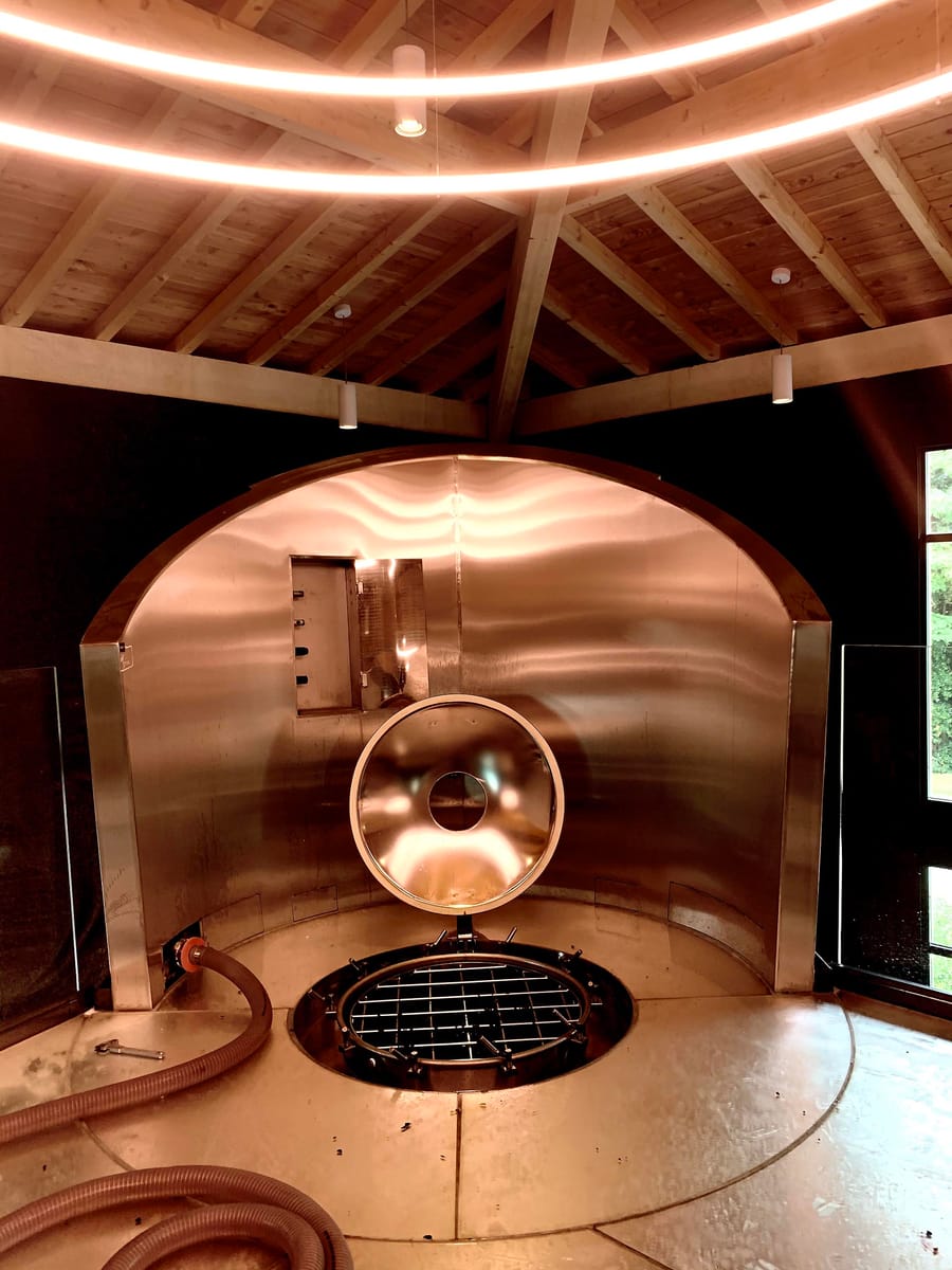 Cuve en inox sous une charpente circulaire en bois avec éclairage suspendu dans un chai viticole à Saint-Émilion