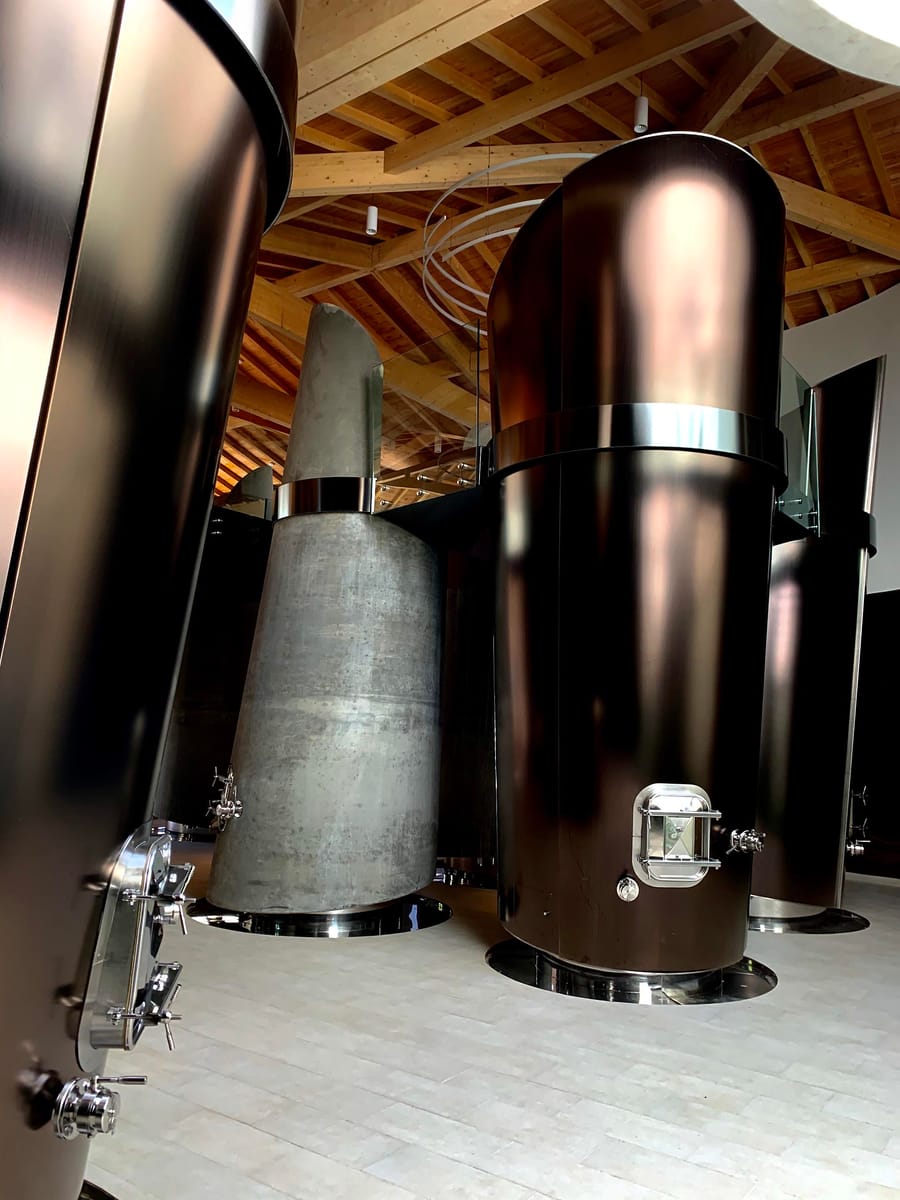 Cuves à vin métalliques et en béton alignées sous une charpente en bois dans un chai contemporain à Montlabert