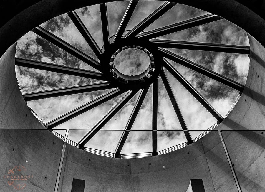 Verrière circulaire à la structure métallique rayonnante ouvrant sur un ciel nuageux, au Château Montlabert