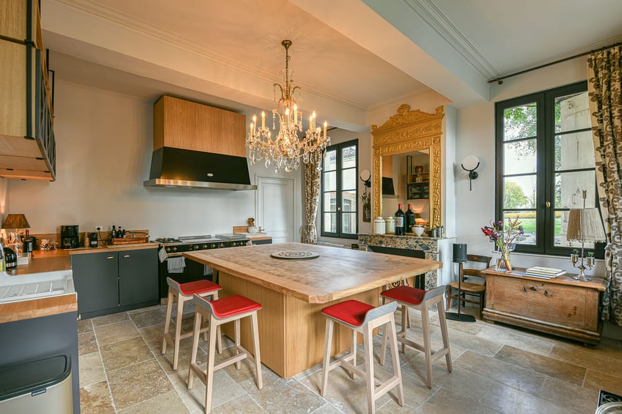 Cuisine aménagée avec grand îlot en bois, tabourets aux assises rouges et lustre en cristal dans une demeure, Château Montlabert à Saint-Émilion