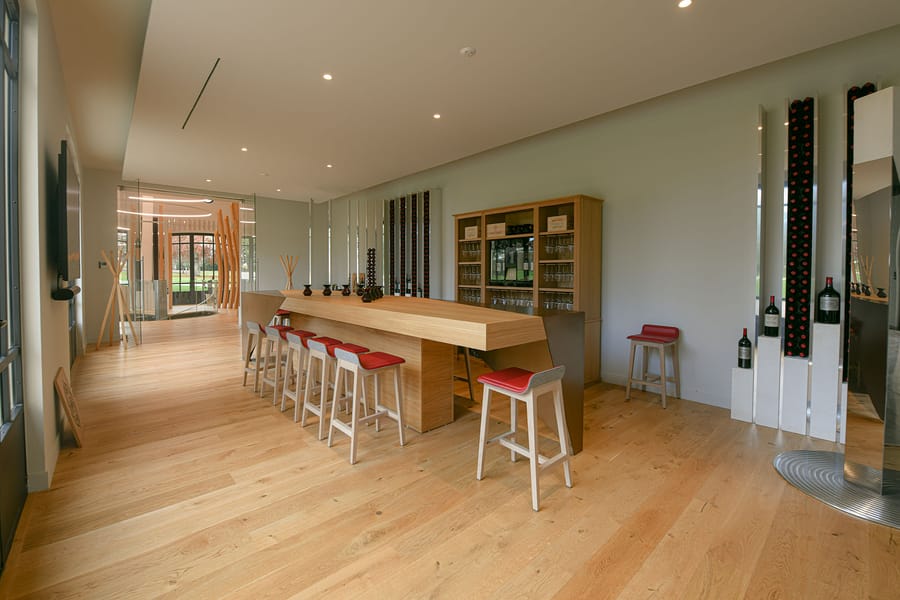 Espace de dégustation contemporain aménagé avec un long comptoir en bois, des tabourets hauts rouges et des bouteilles de vin, Château Montlabert à Saint-Émilion