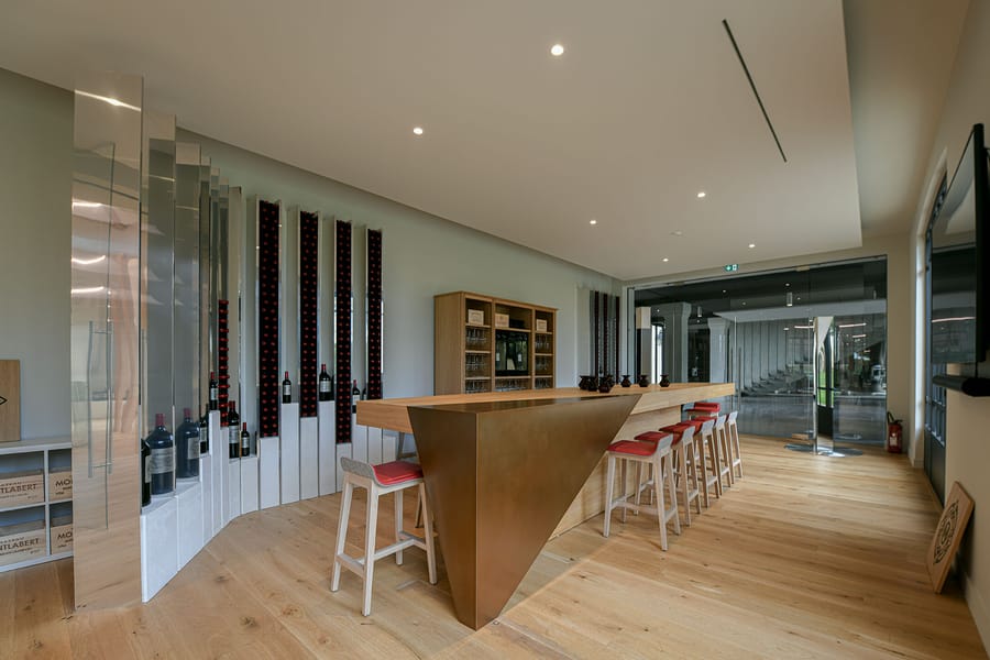 Espace de dégustation contemporain avec comptoir en bois, tabourets hauts et présentoirs à bouteilles de vin, Château Montlabert à Saint-Émilion