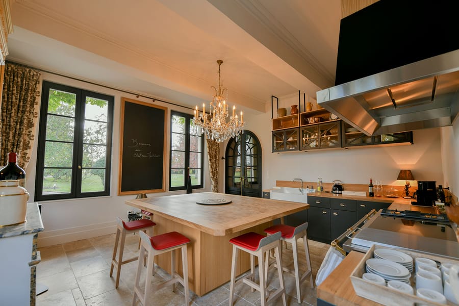 Grande cuisine équipée avec îlot central en bois, tabourets aux assises rouges et lustre en cristal dans une demeure, Château Montlabert à Saint-Émilion