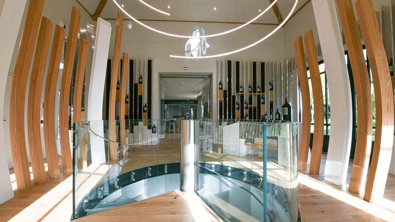 Intérieur contemporain d'une salle de dégustation avec un escalier hélicoïdal, des éléments en bois cintré et des bouteilles exposées, Château Montlabert à Saint-Émilion