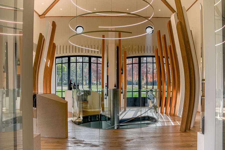 Intérieur contemporain d'une salle de dégustation avec structures en bois, luminaire suspendu circulaire et escalier en verre, Château Montlabert à Saint-Émilion