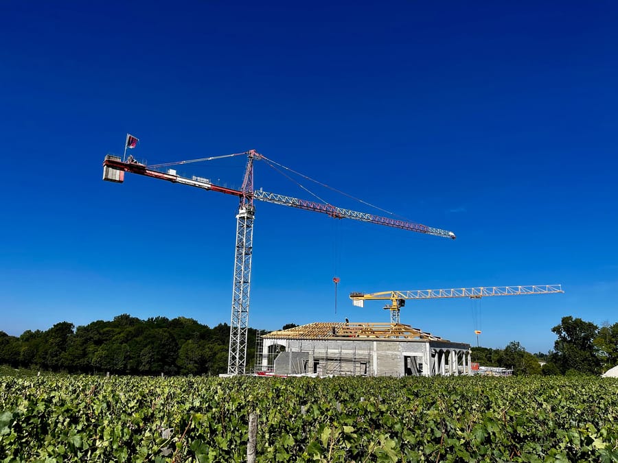 Chantier de construction d'un bâtiment avec deux grues s'élevant au milieu des vignes, Château Plain Point à Fronsac