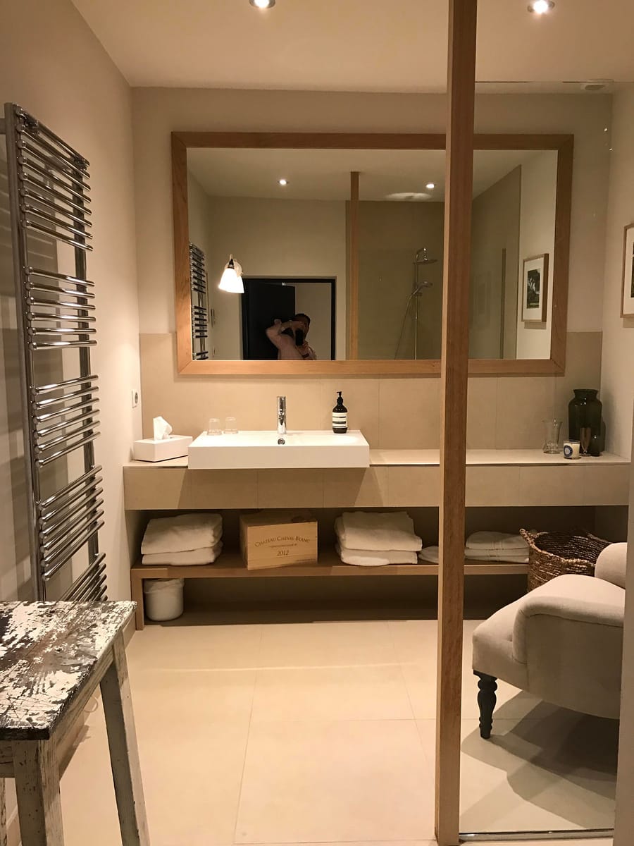 Salle de bains claire avec une vasque blanche, un grand miroir encadré de bois et des rangements bas, Château Tour du Pin à Saint-Émilion
